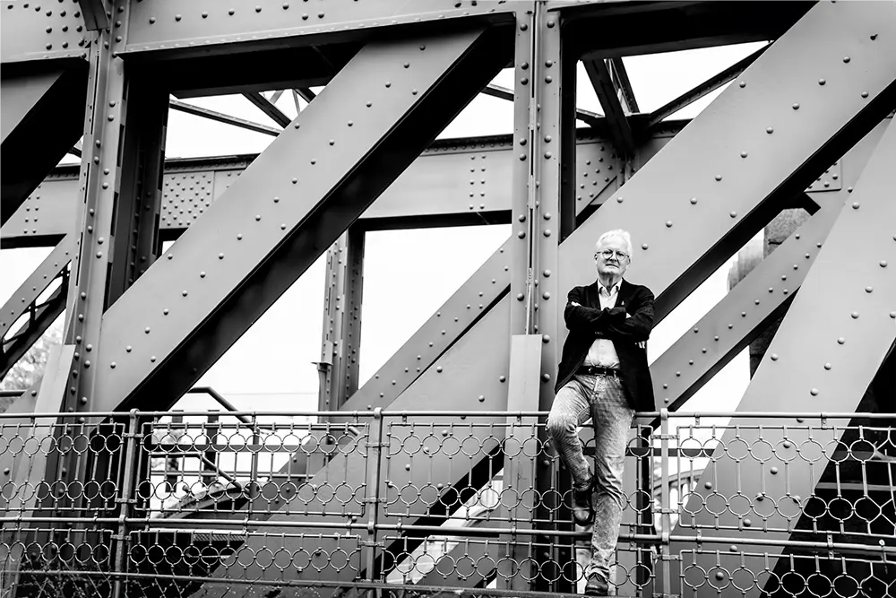 Black and white image of Dr. Erhard Böhm, attorney at law at BOEHM ARBITRATION, leaning against a handrail of the bridge crossing the intake of the Danube Canal in Vienna.