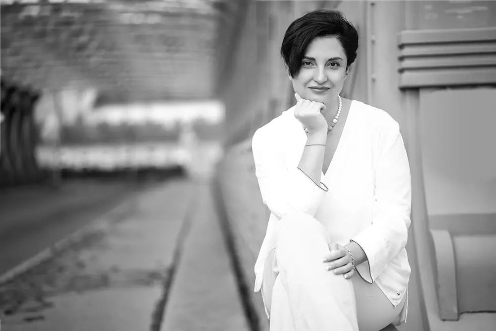 Black and white image of Dr. Irina Nazarova, attorney at law at BOEHM ARBITRATION, sitting at the entrance of the bridge crossing the intake of the Danube Canal in Vienna.