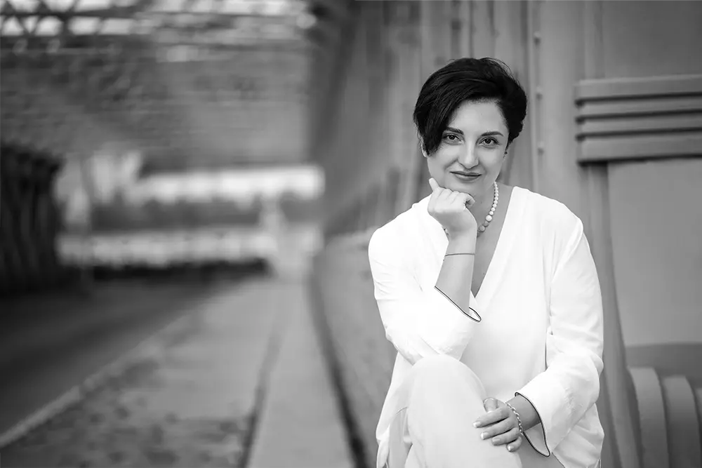 Black and white image of Dr. Irina Nazarova, attorney at law and part of the team at BOEHM ARBITRATION, sitting at the entrance of the bridge crossing the intake of the Danube Canal in Vienna.